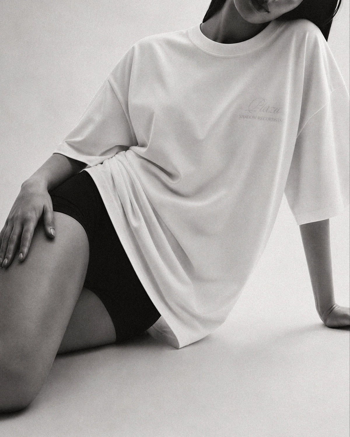 Person wearing a white oversized t-shirt and black shorts on a light background